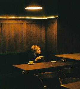 a woman in a dark cafe - no windows dark paneling, holding a coffee 